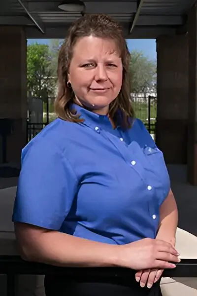 A woman in blue shirt standing outside near a building.